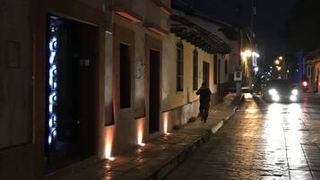 A nighttime street scene with buildings, a person walking, and a car with headlights on.