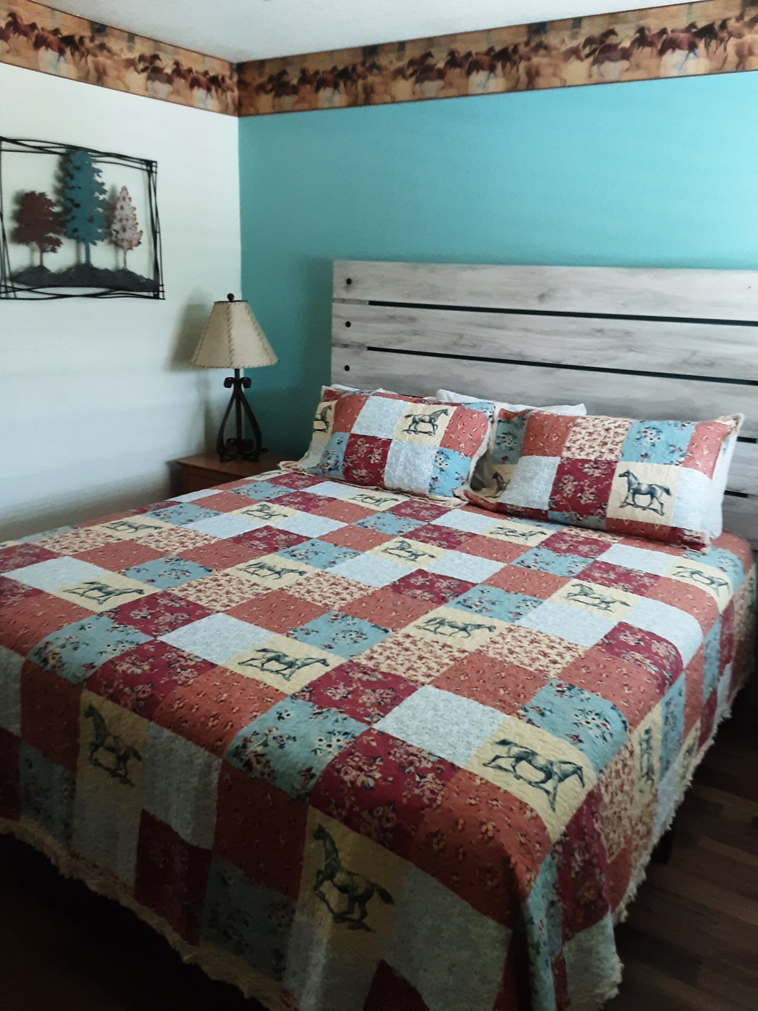 A bed with a quilted bedspread, a wooden headboard, a bedside lamp, and a wall-mounted picture.