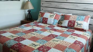 A bed with a quilted bedspread, a wooden headboard, a bedside lamp, and a wall-mounted picture.
