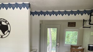 Una habitación con una cama, un escritorio de madera, una silla, una puerta que da al exterior y una pared con un letrero de bienvenida.