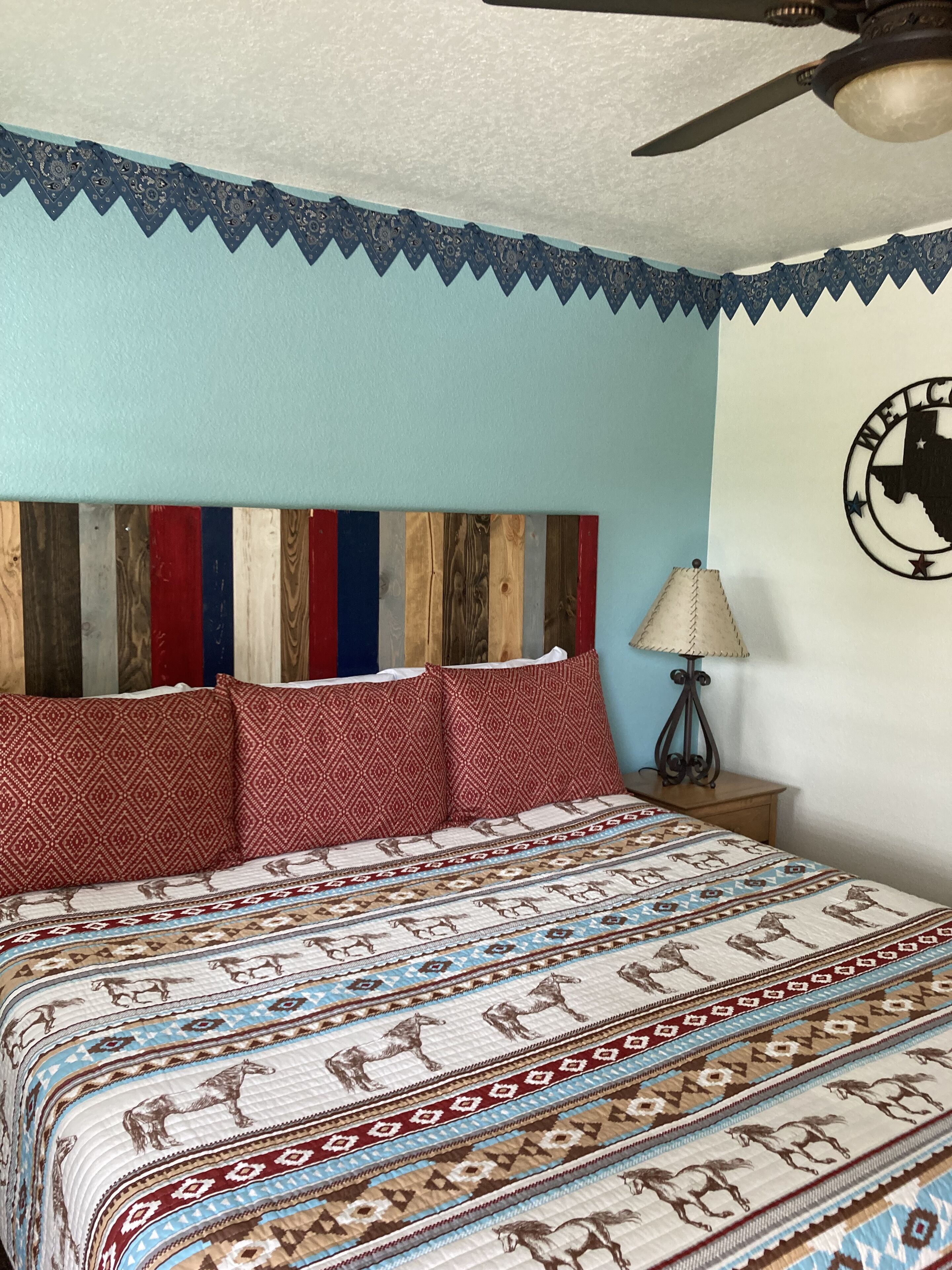 A bedroom with a bed, pillows, a wall clock, and a lamp.