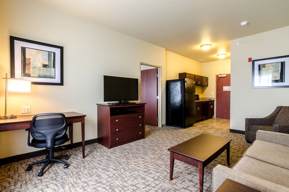 A compact hotel room with a kitchenette, a desk with a chair, a sofa, and a television.