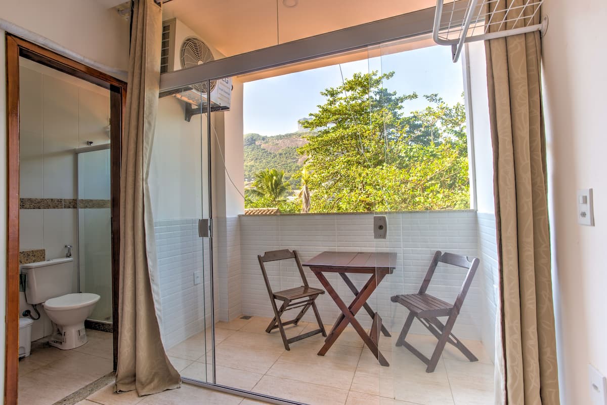Un baño con inodoro, ducha y puerta de vidrio que da a un balcón con mesa y sillas.