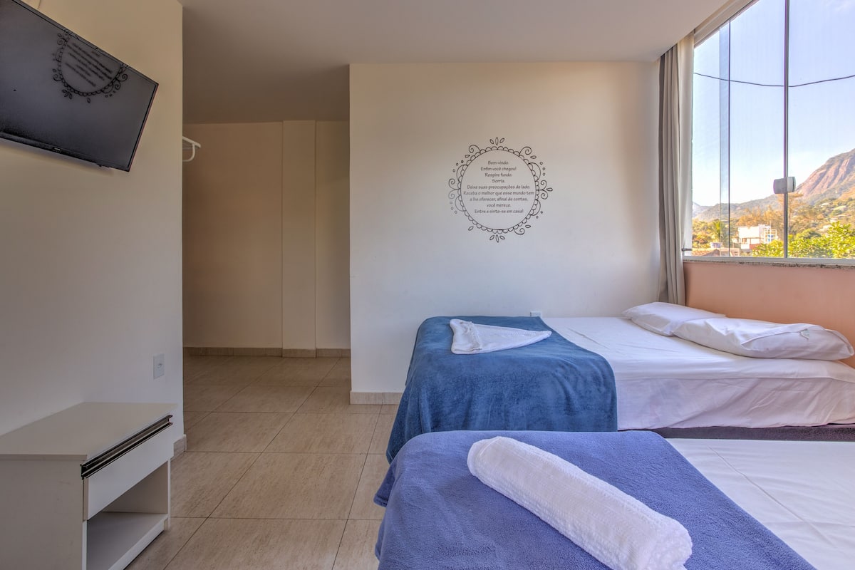Habitación de hotel con dos camas, un televisor de pantalla plana en la pared y vistas a la montaña a través de la ventana.