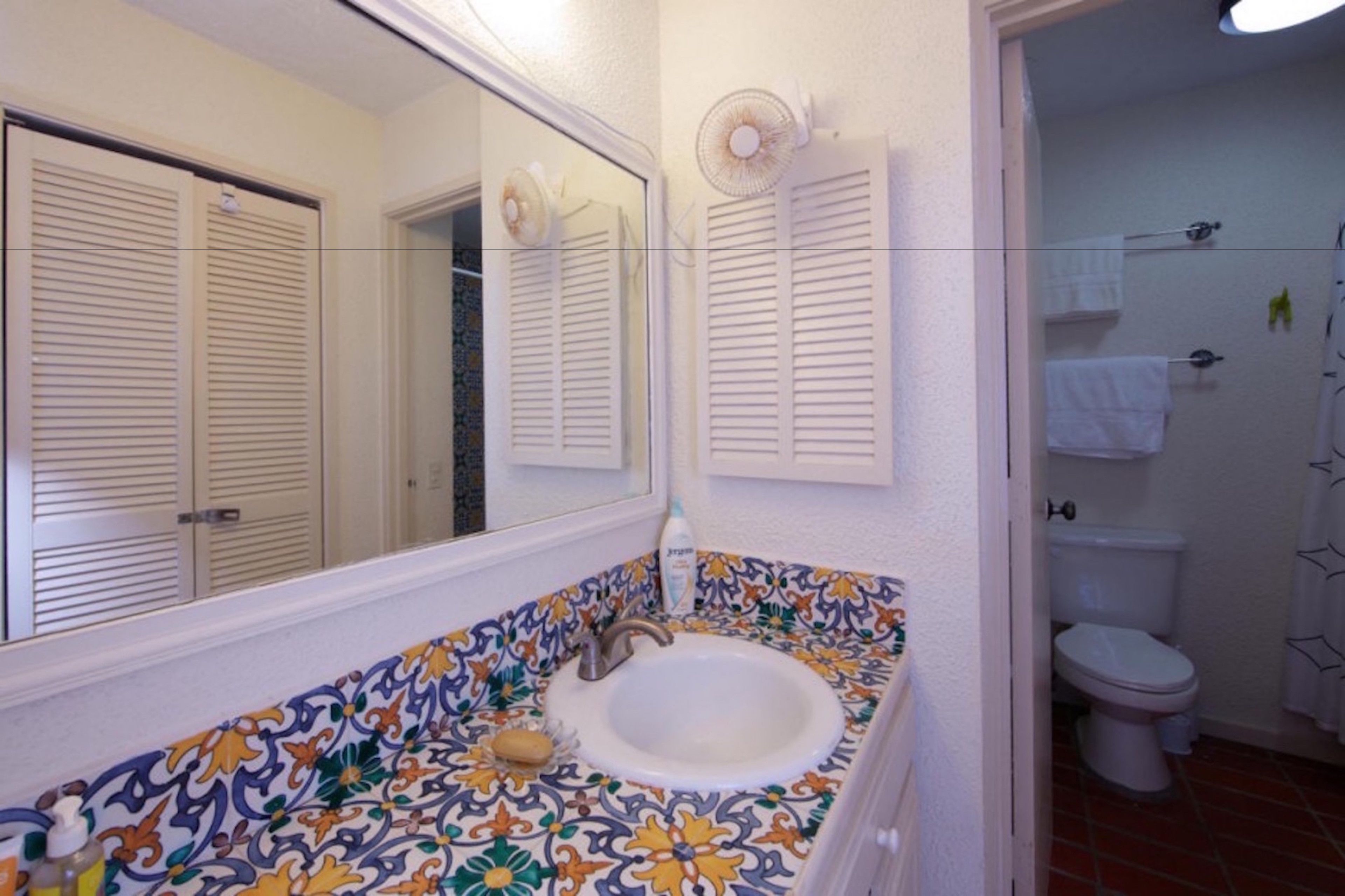 A bathroom with a tiled sink, a mirror, and a toilet.