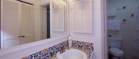 A bathroom with a tiled sink, a mirror, and a toilet.