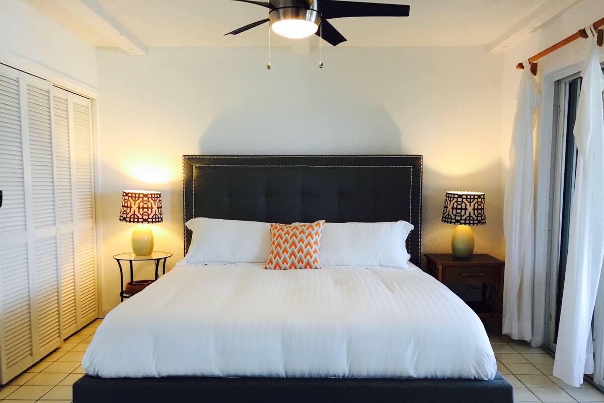 A large bed with a dark headboard, two bedside lamps, and a ceiling fan in a hotel room.