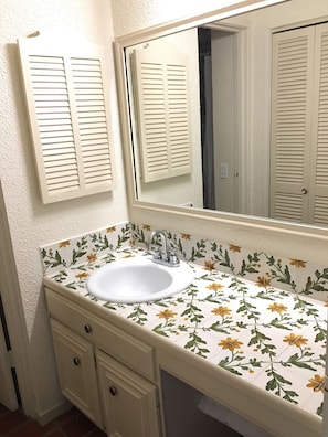 A bathroom with a white sink, a mirror above it, and a door with louvered shutters.
