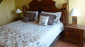 A neatly made bed with a leaf-patterned bedspread, a wooden headboard, and two bedside lamps. - Condo Rusti (Mazatlán)
