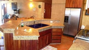 A kitchen with a granite countertop, wooden cabinets, a stainless steel refrigerator, and a built-in sink. - Condo Rusti (Mazatlán)