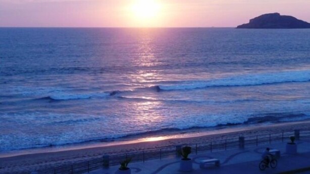 A sunset over the ocean with a beach and a distant island. - Condo Rusti (Mazatlán)