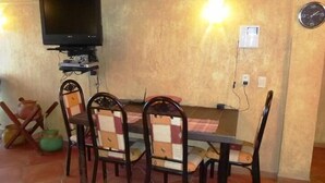 A dining area with a television mounted above a table, surrounded by chairs. - Condo Rusti (Mazatlán)