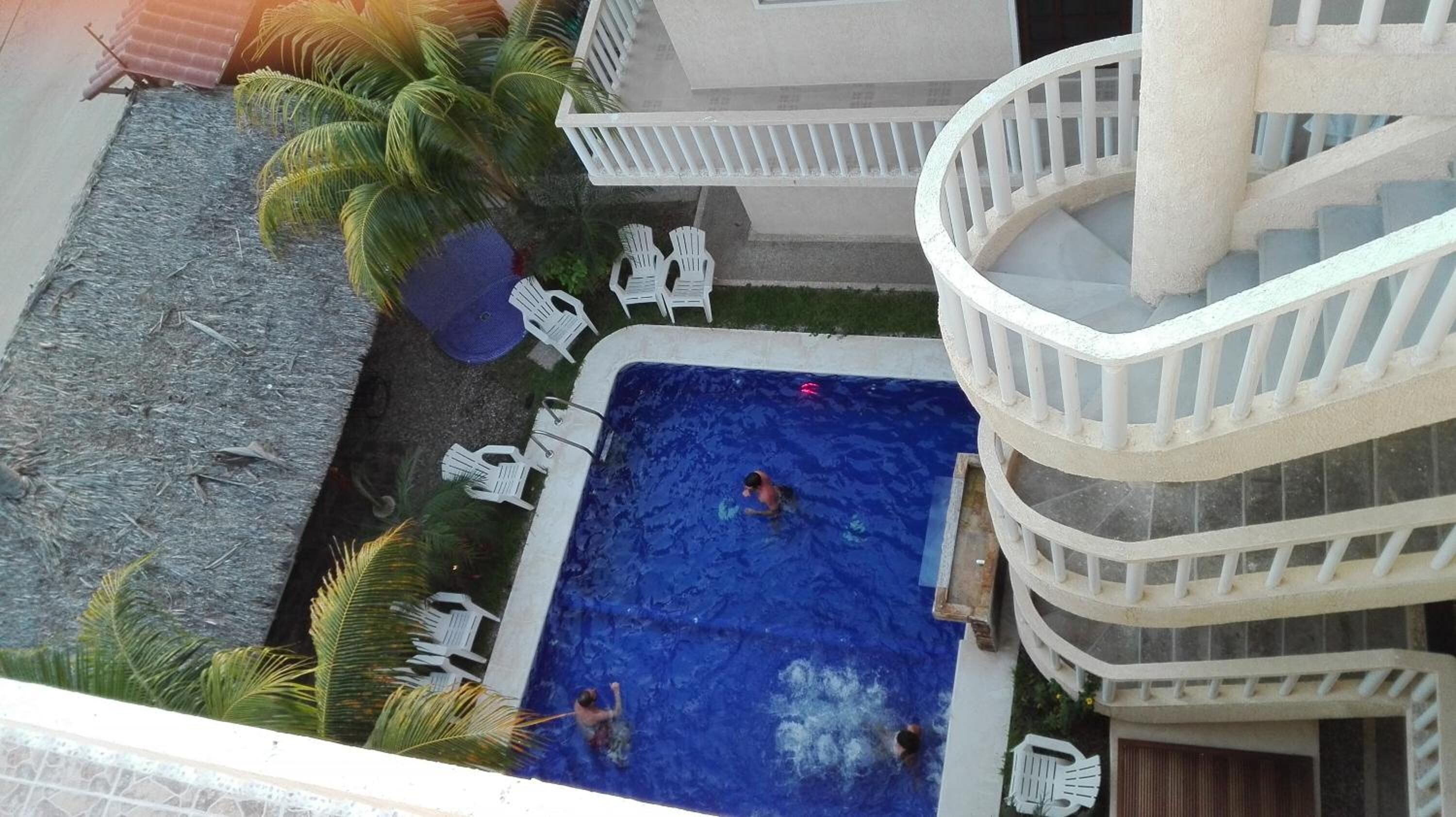 A rooftop pool with multiple levels of balconies, surrounded by palm trees and white chairs.
