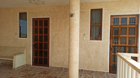 Un pasillo con dos puertas, cada una con un ventanal. Las paredes tienen una textura y el piso, baldosas con diseño.
