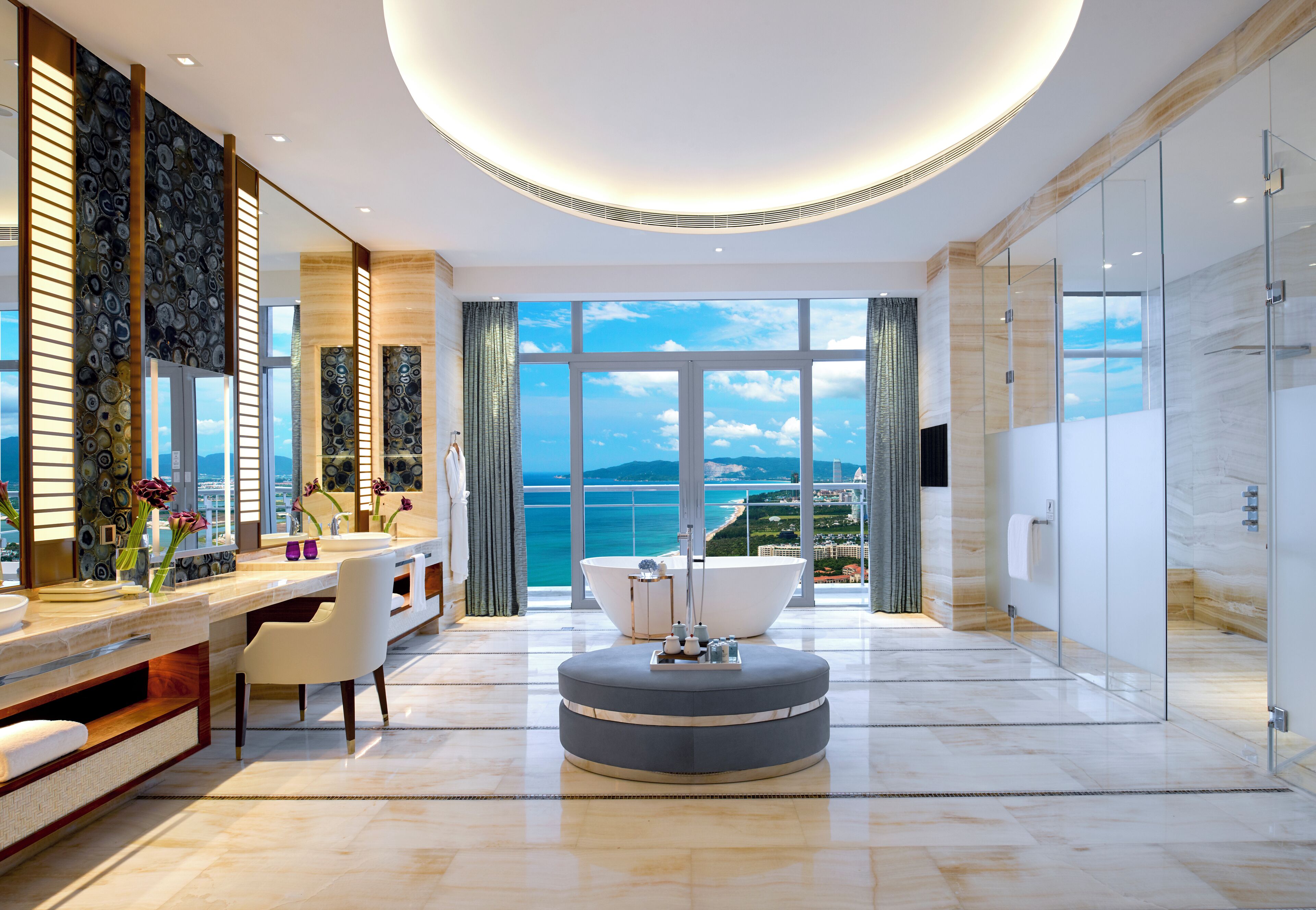 A modern bathroom with a large bathtub, a vanity with a mirror, and a view of the sea.