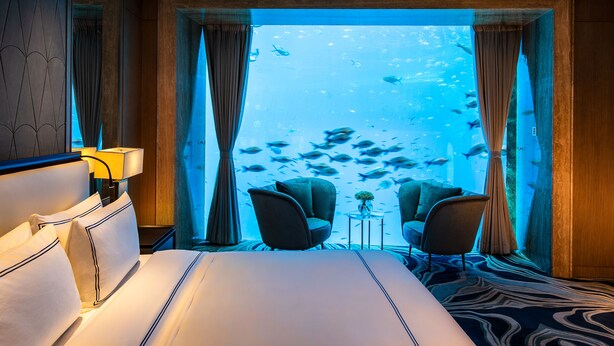 A hotel room with a large bed, two armchairs, a small table, and a view of an aquarium with fish. - Atlantis Sanya (Sanya)