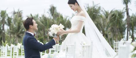 A wedding ceremony with a groom kneeling and presenting a bouquet to the bride.