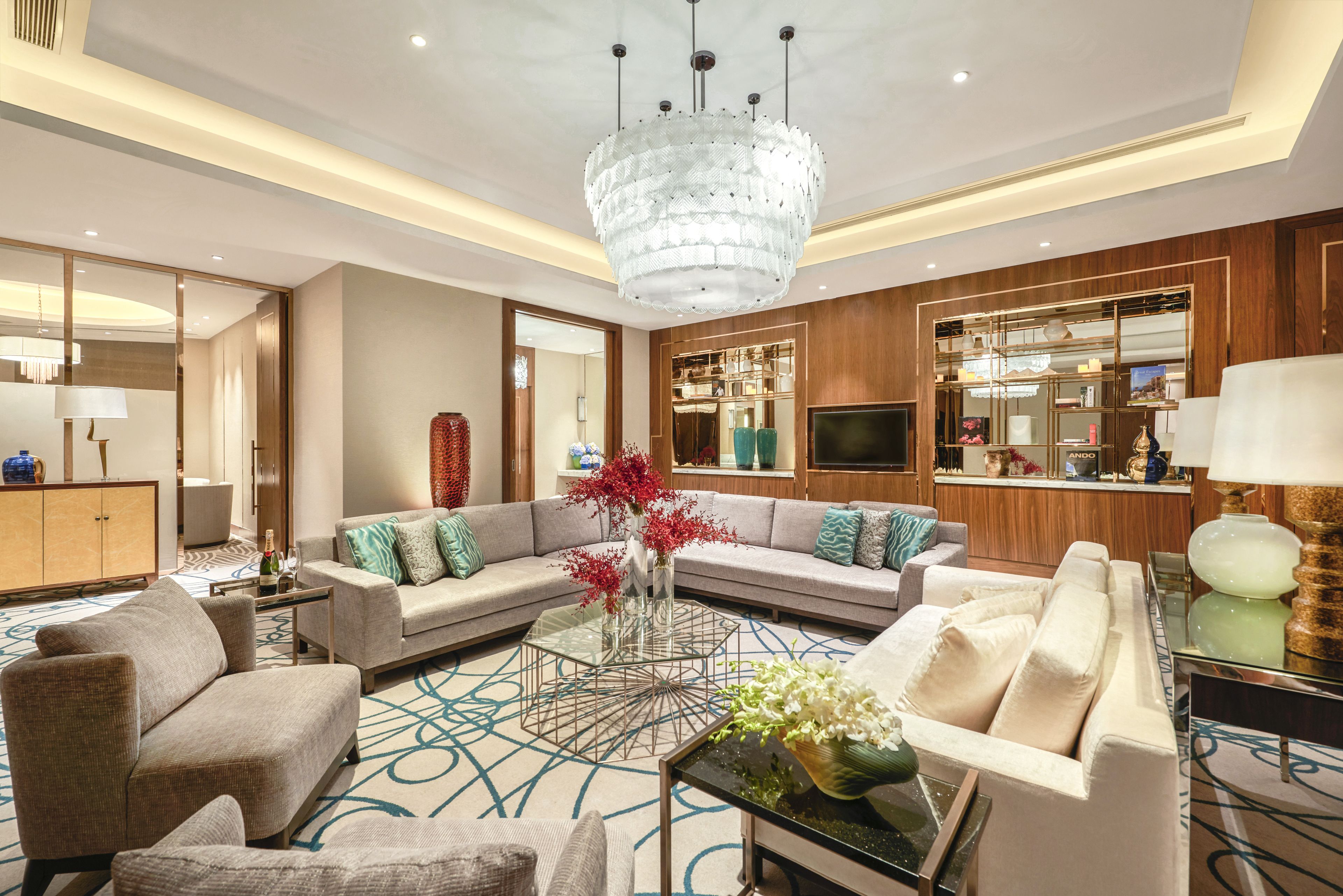 A spacious living room with a modern chandelier, sofas, a coffee table, and a TV.