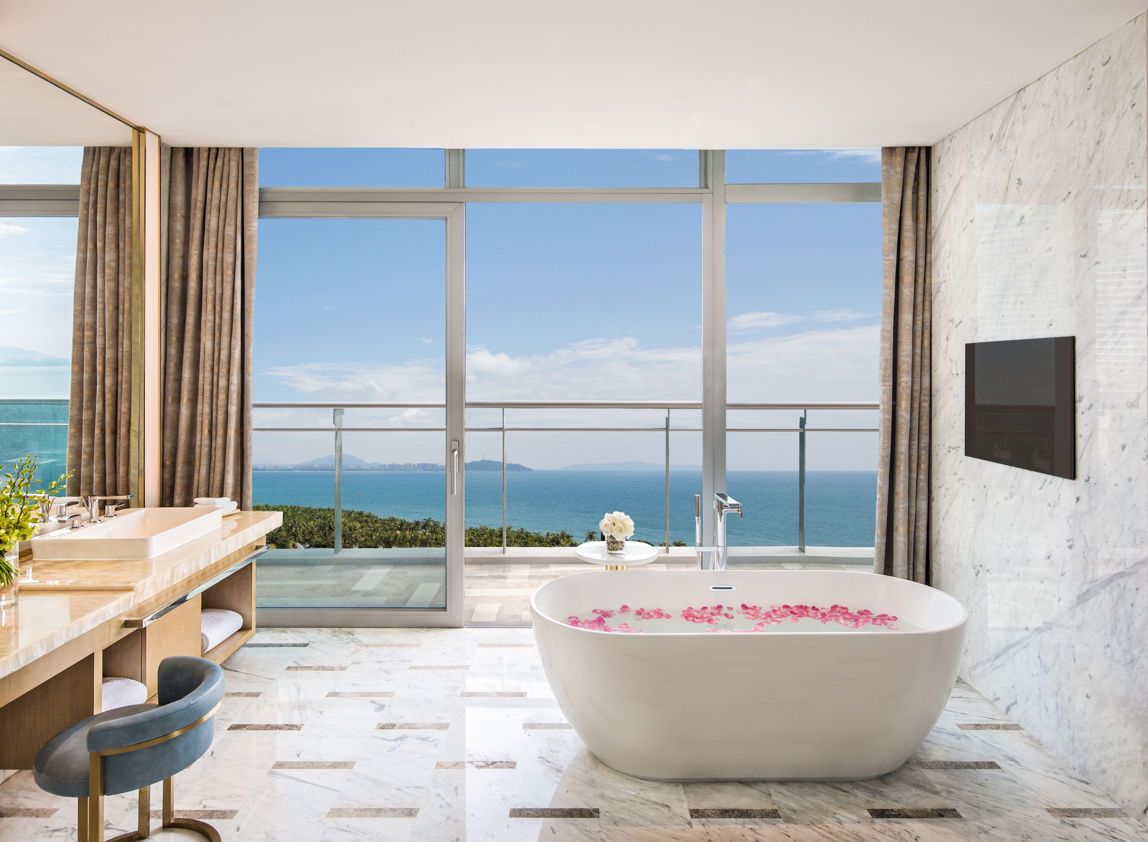 A modern bathroom with a large bathtub, a vanity with a mirror, and a view of the sea.