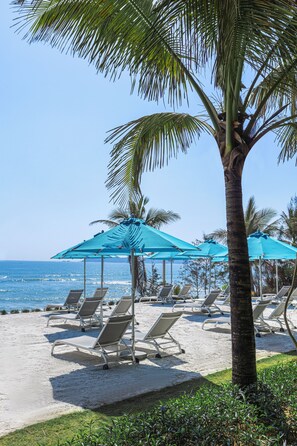 A beachside area with lounge chairs and umbrellas, a palm tree, and the ocean in the background. - Atlantis Sanya (Sanya)