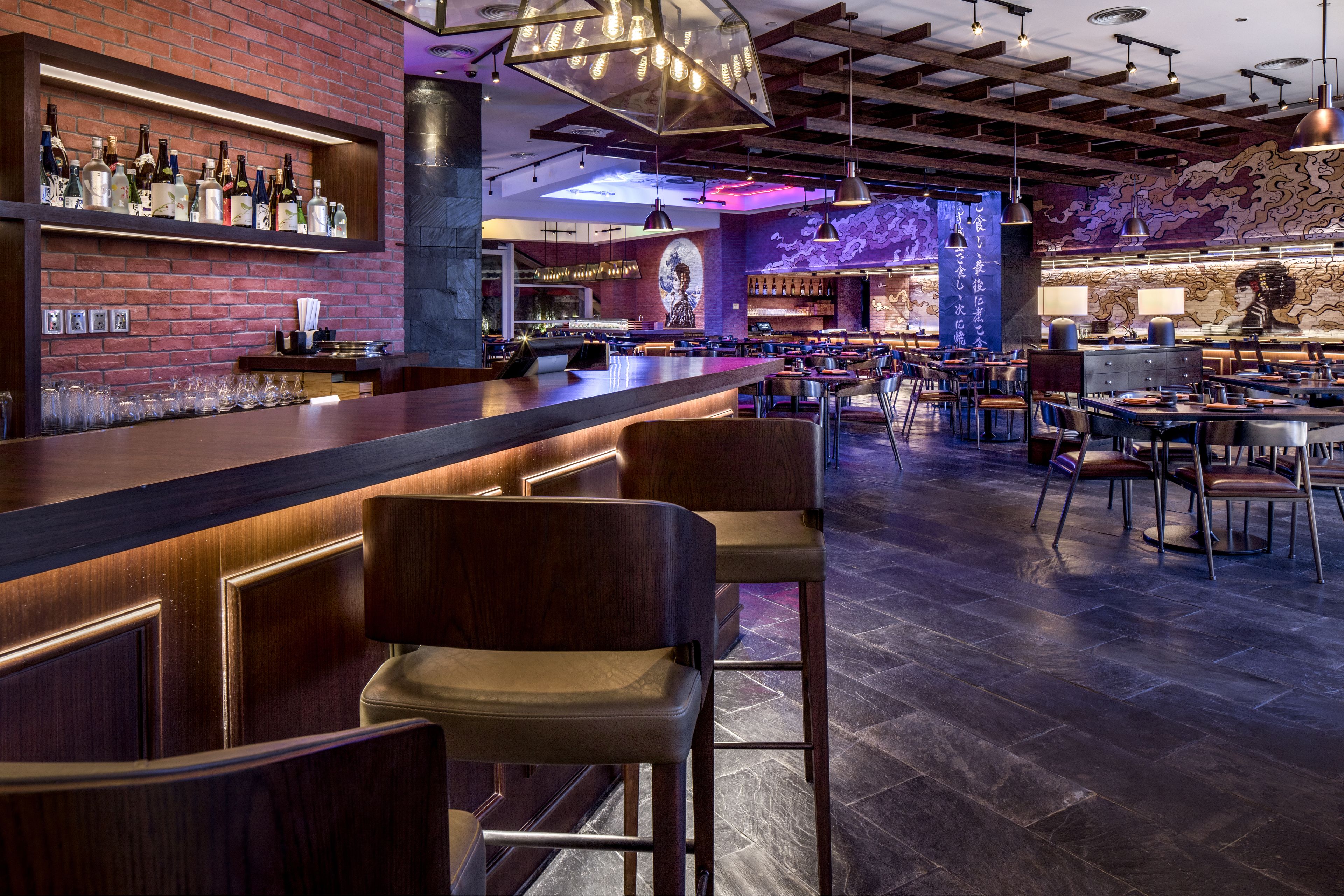 A bar area with a long counter, multiple stools, and a variety of bottles on shelves.