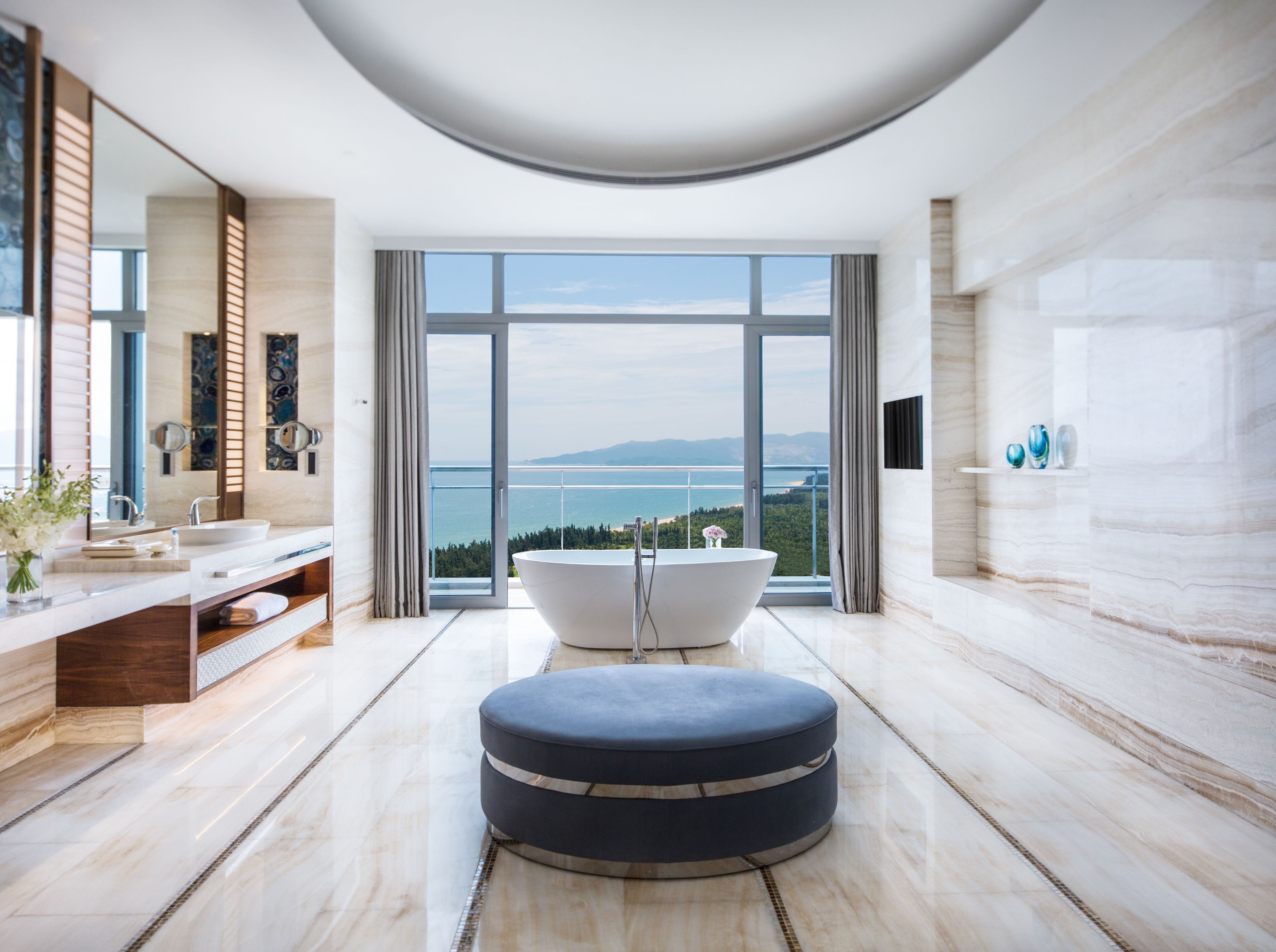 A modern bathroom with a large bathtub, a vanity with a mirror, and a view of the sea.