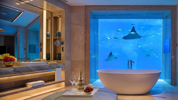 A modern bathroom with a large bathtub, a vanity with a mirror, and an aquarium with fish and stingrays. - Atlantis Sanya (Sanya)