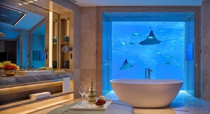 A modern bathroom with a large bathtub, a vanity with a mirror, and an aquarium with fish and stingrays. - Atlantis Sanya (Sanya)