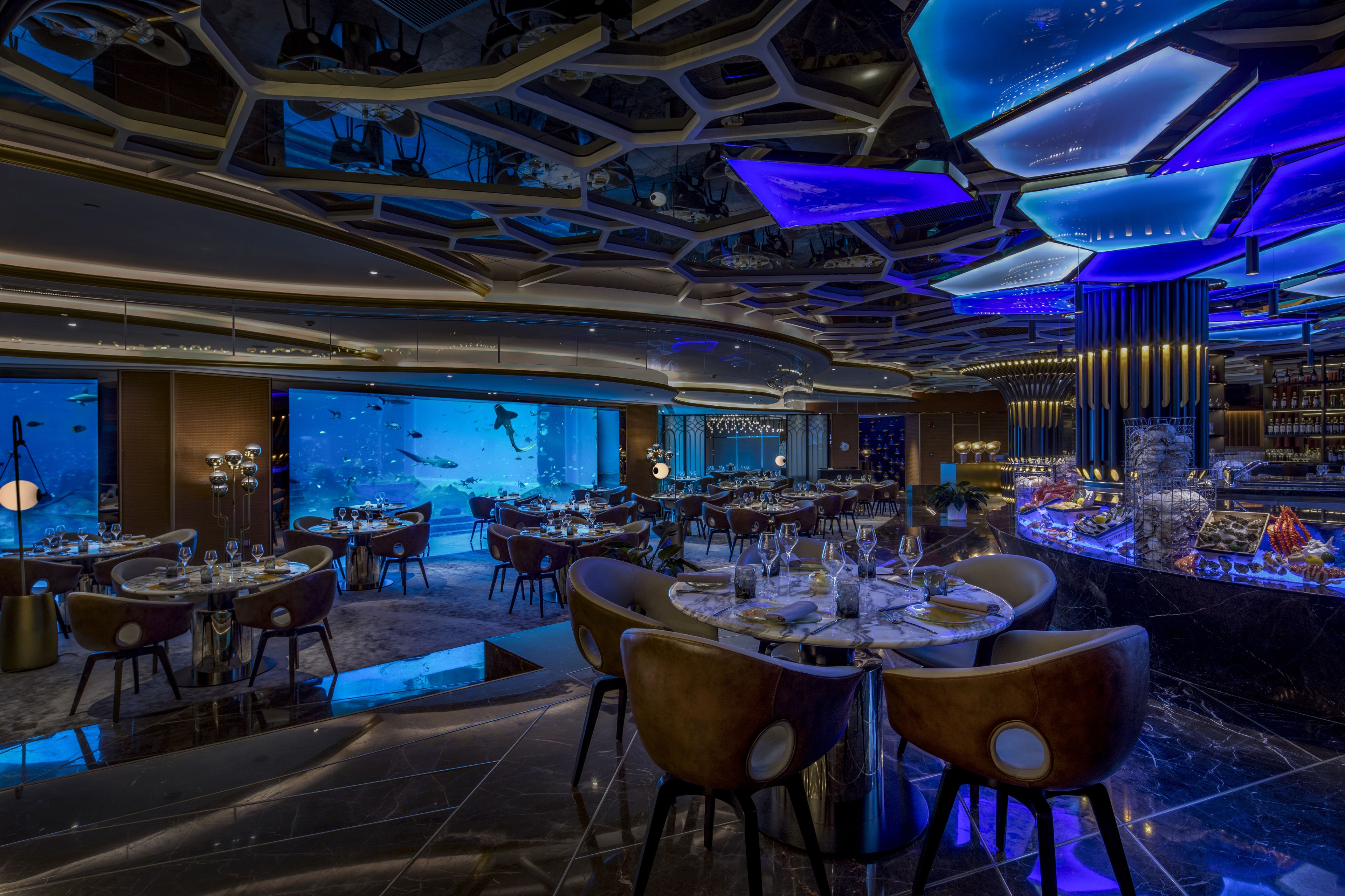 A modern restaurant with a unique ceiling design, underwater aquarium views, and a variety of seating arrangements.