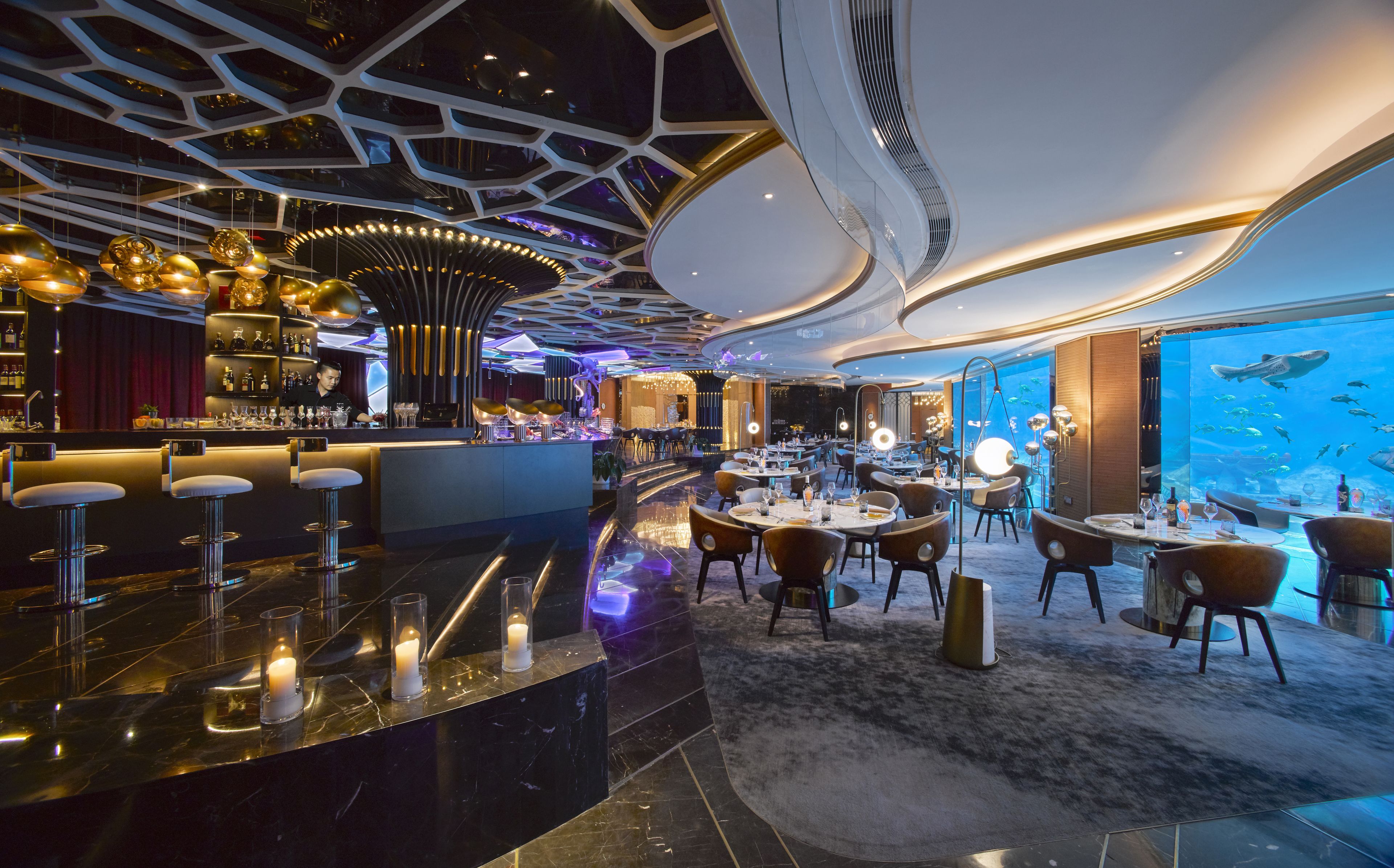 Un restaurante moderno con barra, asientos y una pared con acuario.