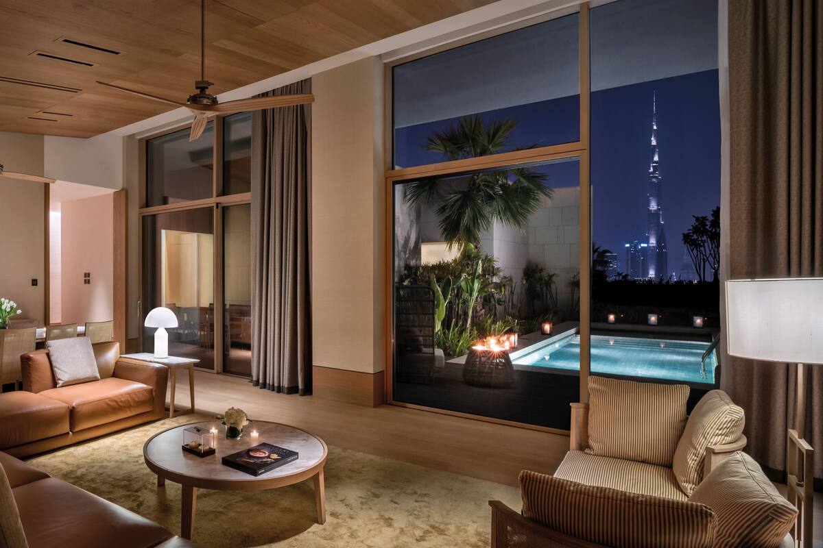 A modern living room with a large window overlooking a pool and a city skyline at night.