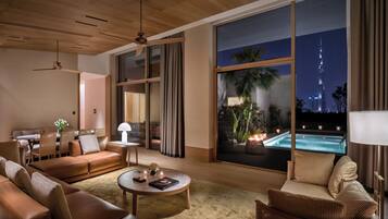 A modern living room with a large window overlooking a pool and a city skyline at night.