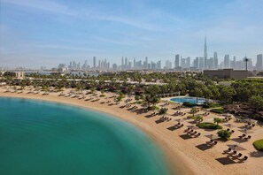 A beach resort with sun loungers, a pool, and a view of the city skyline. - Bvlgari Resort Dubai (Dubai)