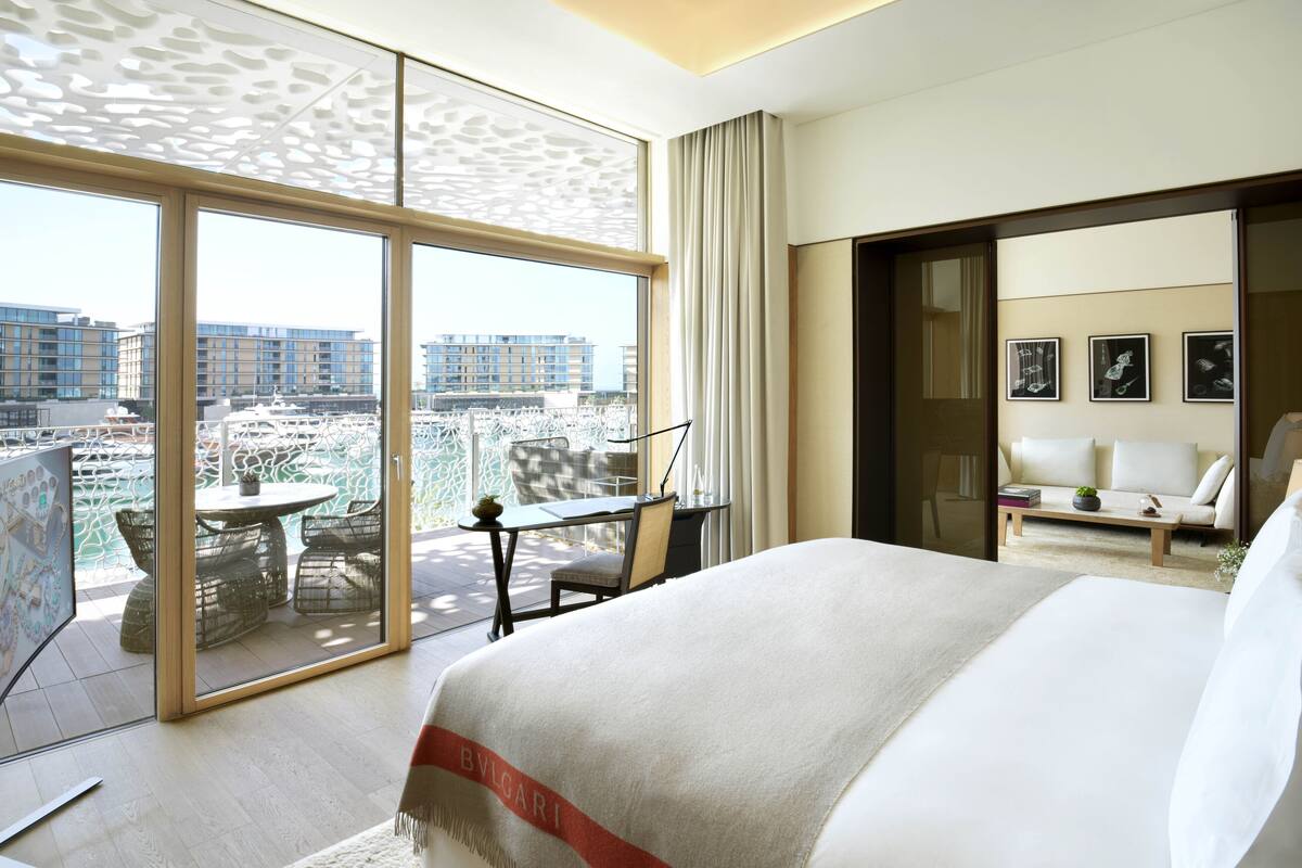 A hotel room with a large bed, a balcony with a table and chairs, and a city view.