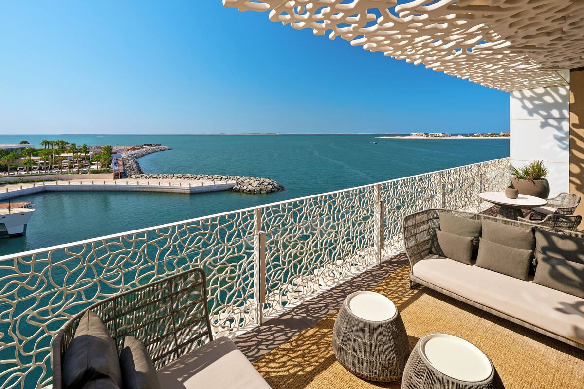 A balcony with a view of the sea, a sofa, a round table, and a potted plant.