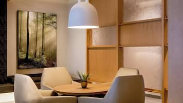 Un interior moderno con una mesa redonda de madera, dos sillas con cojines, una lámpara colgante blanca y un cuadro grande con motivos forestales en la pared.