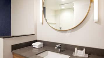 A modern bathroom with a large mirror, a sink, and a towel stack.