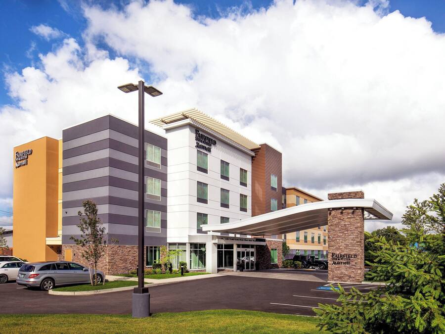 Et Fairfield Inn & Suites hotel med moderne design, der inkluderer en stor parkeringsplads og en overdækket indgang.