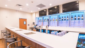 A bar area with a long counter, multiple seating options, and shelves displaying bottles and glasses. - Fairfield Inn & Suites by Marriott Brownsville North (Brownsville)