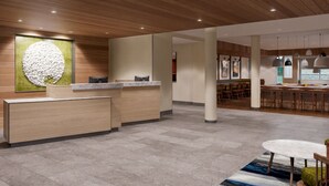 A modern reception area with a wooden reception desk, a large abstract artwork, and a seating area with tables and chairs. - Fairfield Inn & Suites by Marriott Brownsville North (Brownsville)
