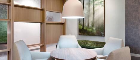 A modern interior with a round wooden table surrounded by light-colored chairs, a hanging pendant light, and a large forest-themed painting on the wall.