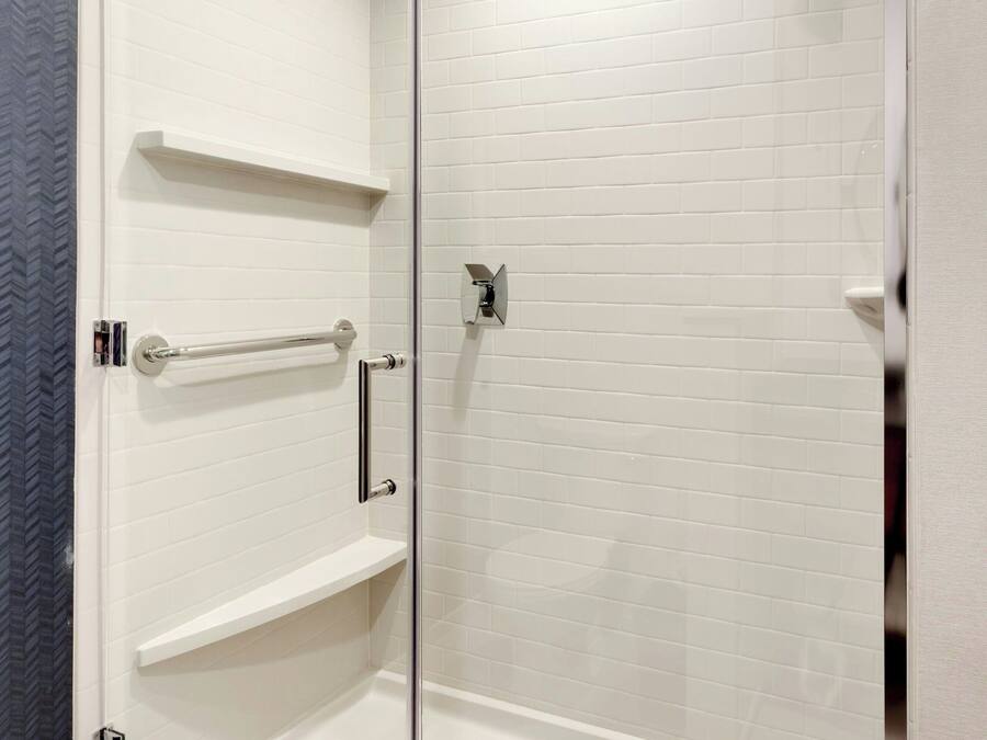 A modern shower area with glass doors, white tiled walls, and a built-in showerhead.