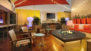 Un espace de détente moderne avec des meubles en osier, un foyer central et un éclairage d’ambiance.