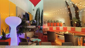 Un espace de détente intérieur aménagé avec des meubles en osier, un foyer et des guirlandes lumineuses.