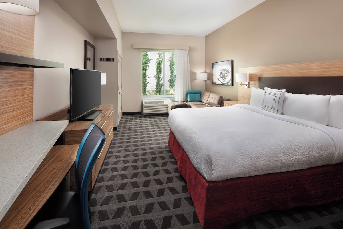 A hotel room with a bed, desk, chair, TV, and a window with a view of trees.