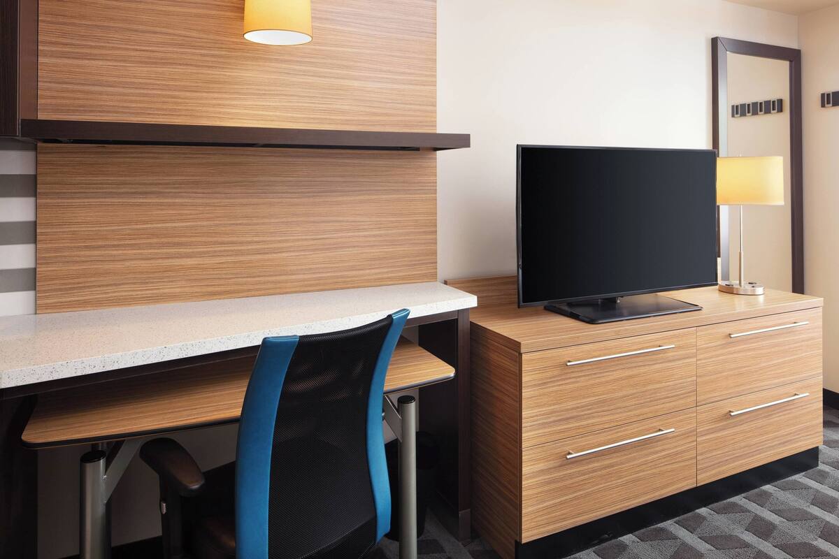 A modern hotel room with a wooden desk, a television, and a mirror.
