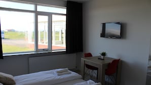 A hotel room with two beds, a TV, a small table with a chair, and a window with a view of the outside.