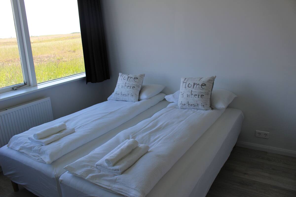 Ein Zimmer mit zwei Betten, jeweils mit weißen Bettwäsche und Kissen, und einem Fenster mit Blick auf ein Feld.