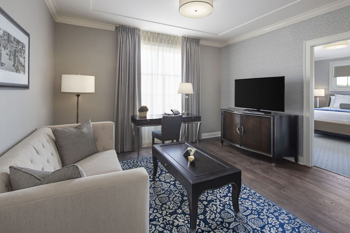 A hotel room with a sofa, a desk with a lamp, a television, and a patterned rug.