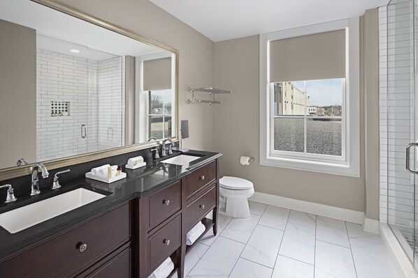 A modern bathroom with two sinks, a large mirror, and a window providing a view of the outside.